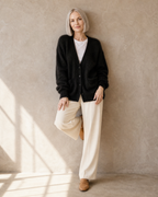 Women's V-Neck Button Cardigan with Pockets in Black, back to wall, knee bent, worn by model