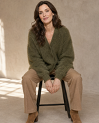 Women's V-Neck Button Cardigan with Pockets in Army Green, perched on stool edge, worn by model