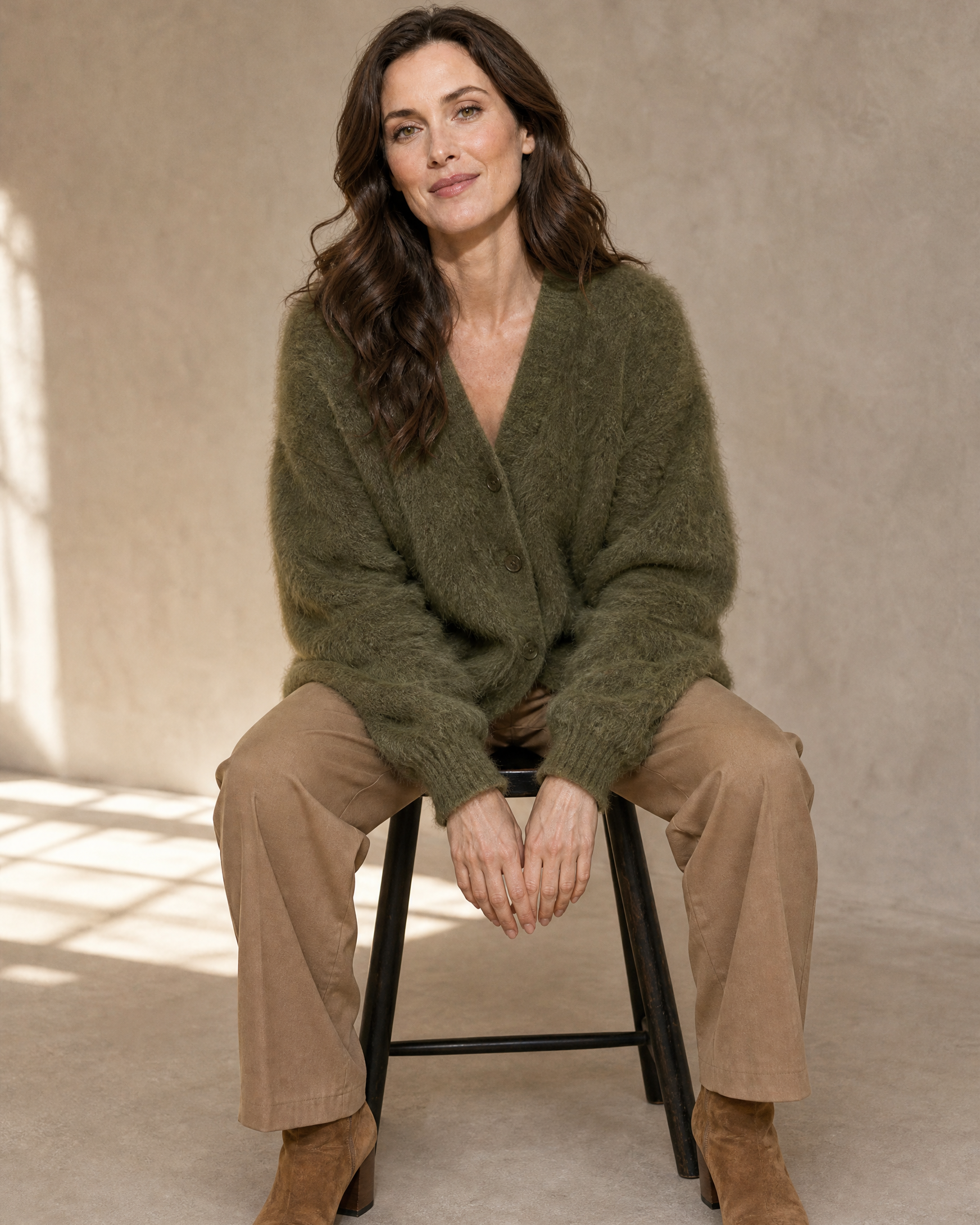 Women's V-Neck Button Cardigan with Pockets in Army Green, perched on stool edge, worn by model