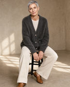 Women's Fuzzy Button Cardigan with Patch Pockets in Grey, perched on stool edge, worn by model