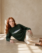 Women's Relaxed Fish Motif Knit Sweater in Dark Green, floor, propped on elbow, worn by model