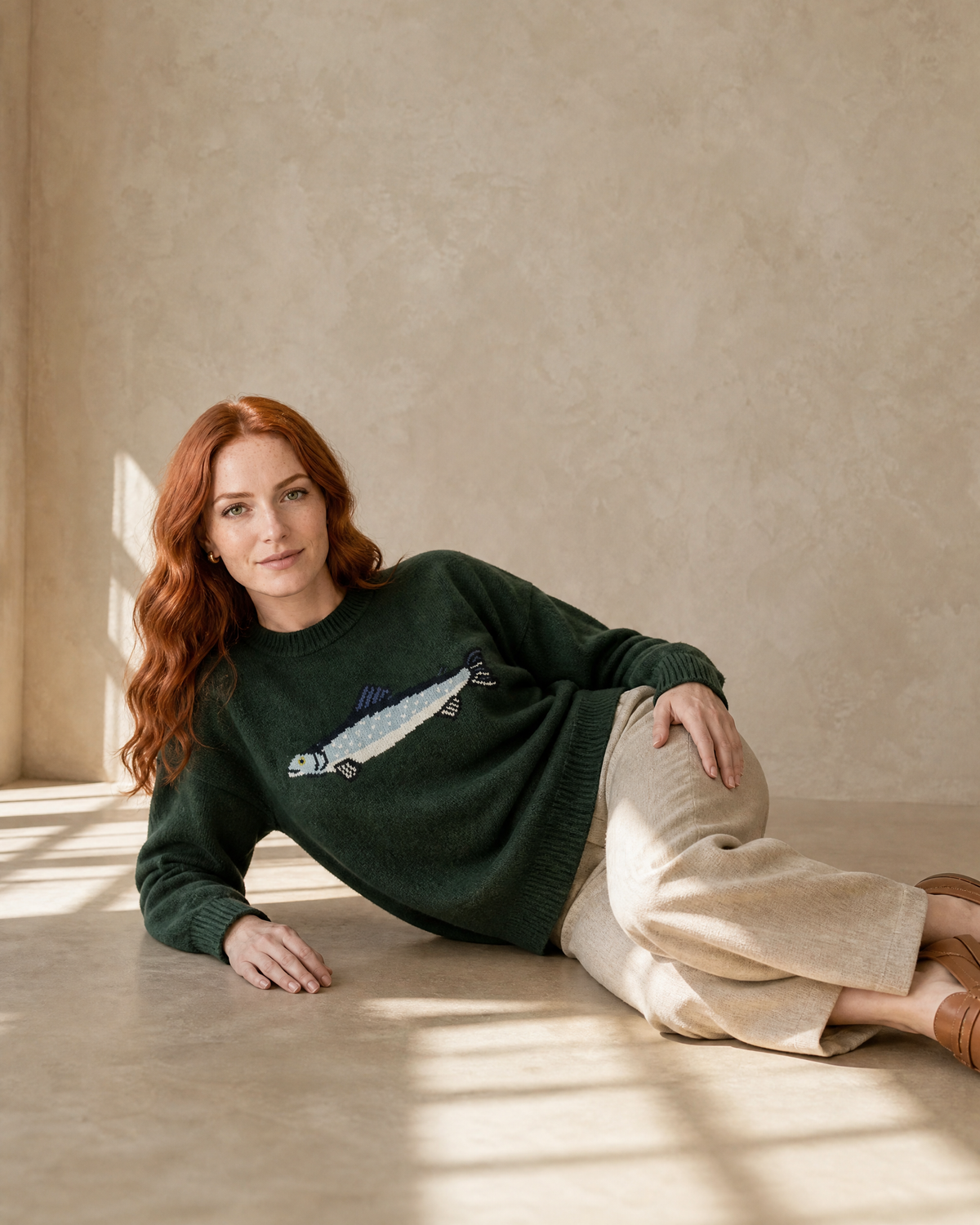 Women's Relaxed Fish Motif Knit Sweater in Dark Green, floor, propped on elbow, worn by model