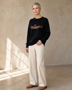 Women's Relaxed Fish Motif Knit Sweater in Black, half turn, hand at hem, worn by model