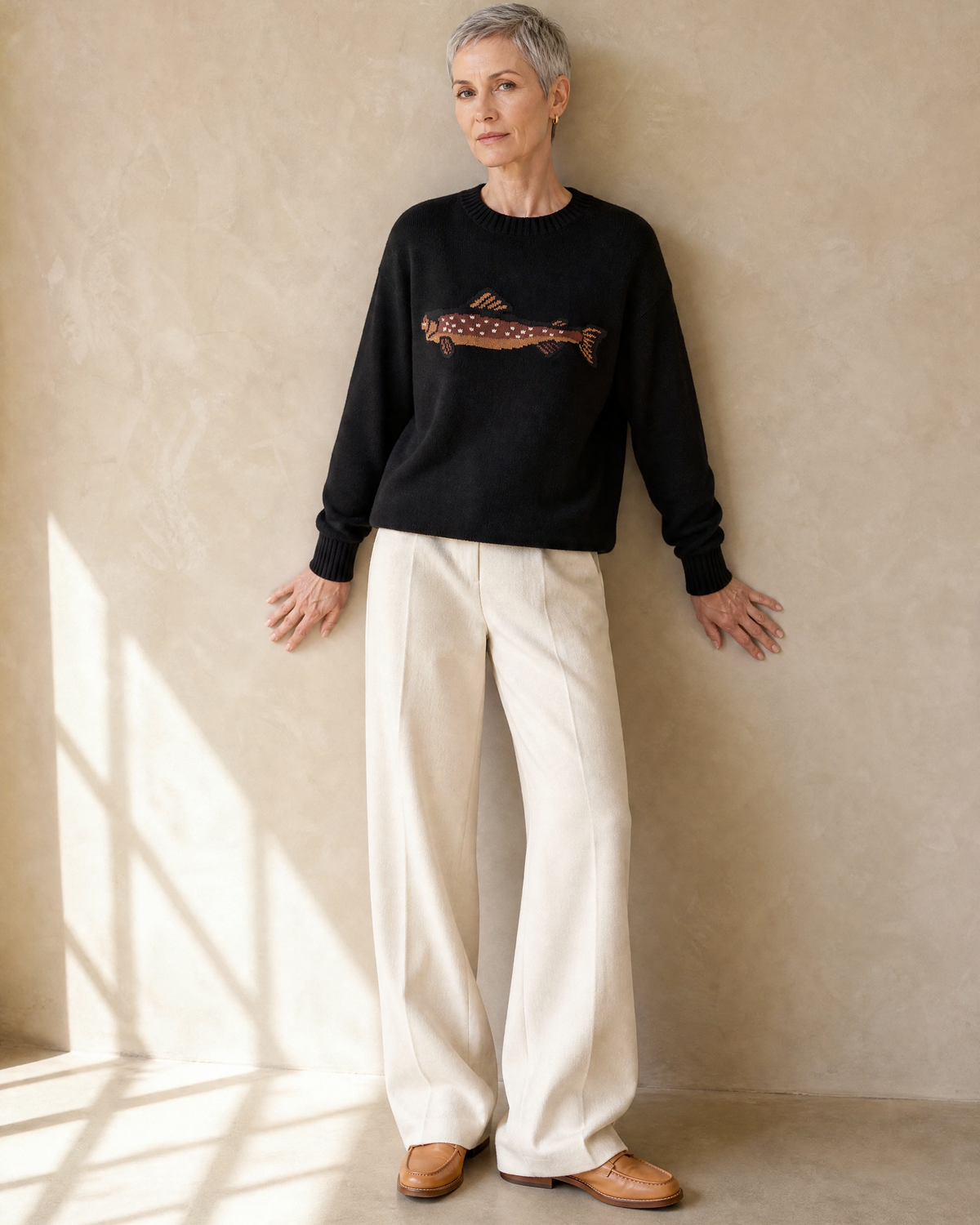 Women's Relaxed Fish Motif Knit Sweater in Black, back against wall, head turned, worn by model